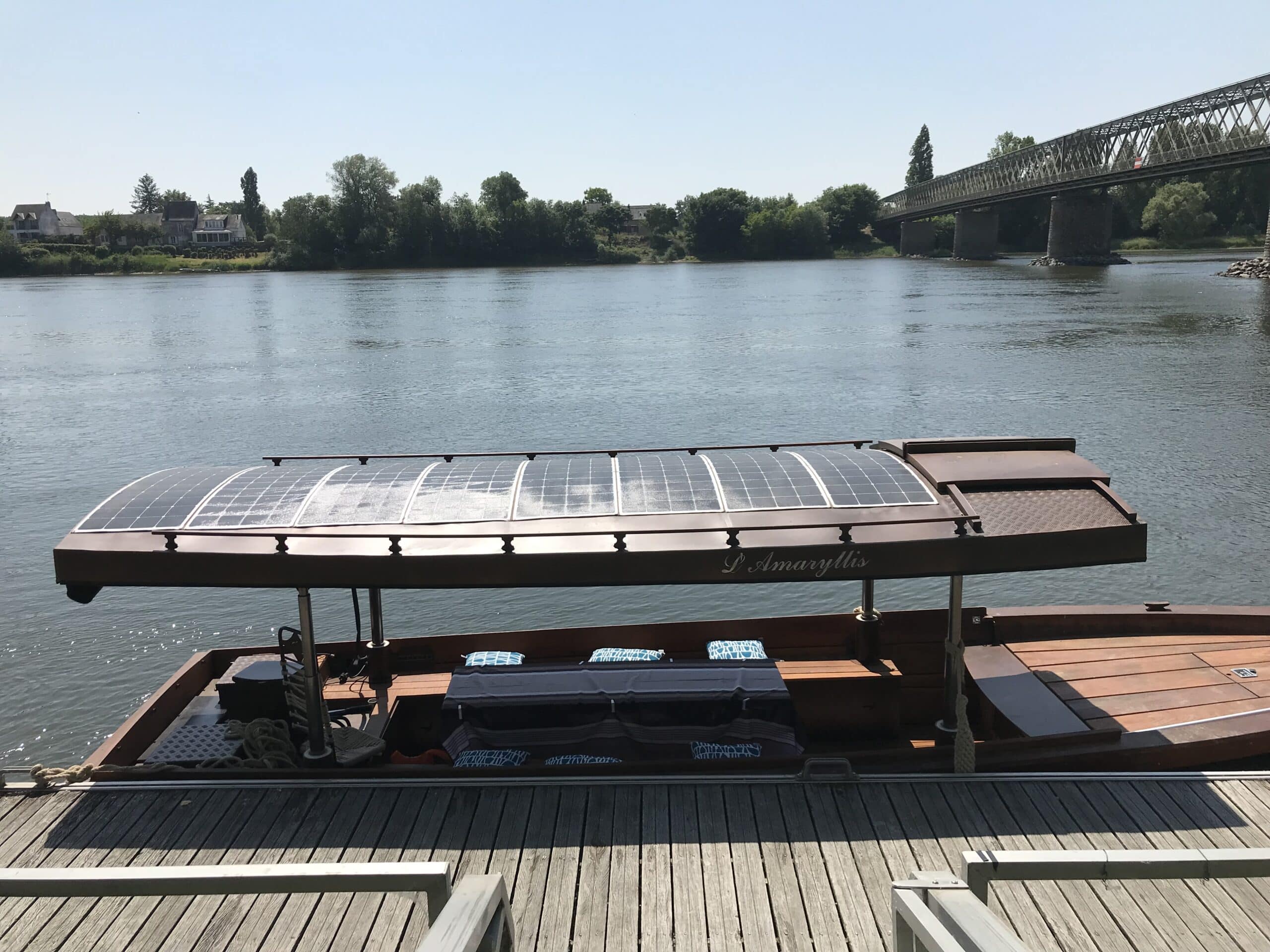 Bateau solaire amarré sur fleuve, pont en bois.