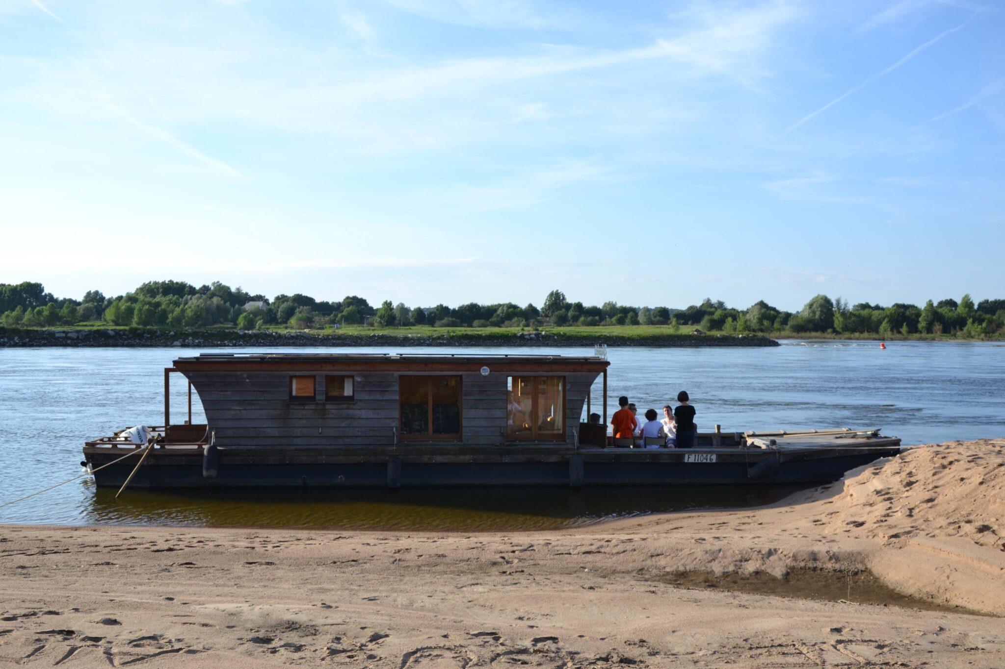 Péniche et personnes sur rive fleuve.